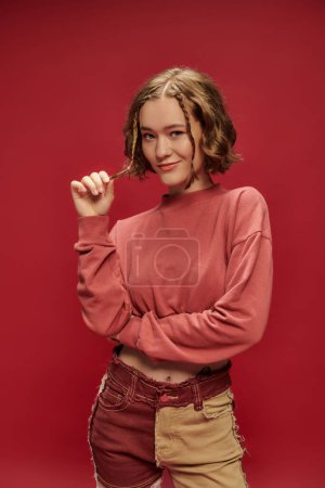 Photo for Personal style, pretty gen z woman in patchwork pants and cropped long sleeve gesturing on red - Royalty Free Image