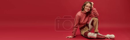 banner of cheerful woman in patchwork pants and cropped long sleeve sitting on red backdrop