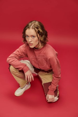 overhead view, stylish gen z girl in patchwork pants and cropped long sleeve on red backdrop