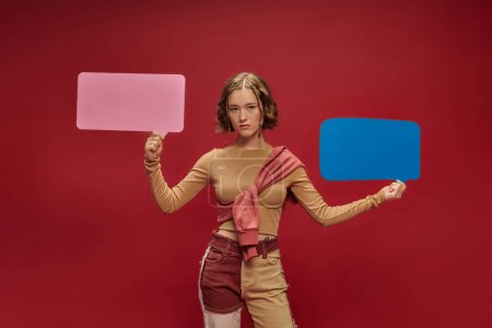 Photo for Stylish young woman in patchwork pants and jumper over cropped long sleeve holding speech bubbles - Royalty Free Image