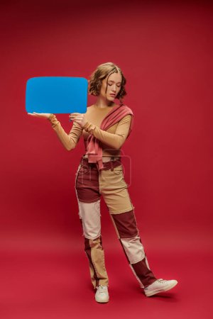 Téléchargez les photos : Jeune femme élégante en patchwork pantalon et pull sur recadré manches longues tenant bulle de parole - en image libre de droit
