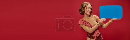 Photo for Banner of happy woman in patchwork pants and jumper over cropped long sleeve holding speech bubble - Royalty Free Image
