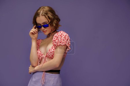 pretty young woman in cropped top with hearts and skirt adjusting sunglasses on purple