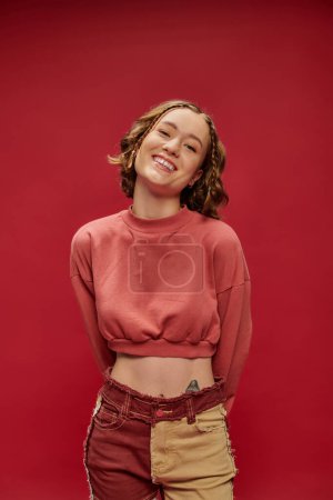 Photo for Happy face, tattooed fashion model posing in patchwork pants and cropped long sleeve on red backdrop - Royalty Free Image