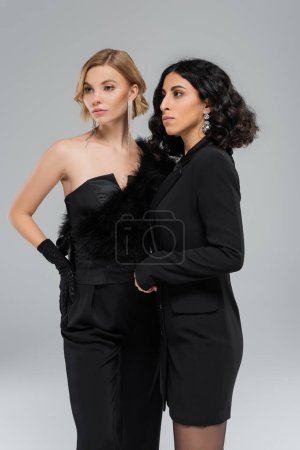 multiracial fashion models in total black elegant attire posing on grey, beauty in diversity