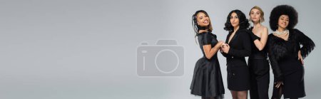 Photo for Happy african american woman holding hands of stylish model near elegant girlfriends on grey, banner - Royalty Free Image