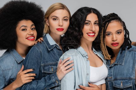 Photo for Group portrait of multiethnic girlfriends in denim wear looking at camera on grey, diverse beauty - Royalty Free Image