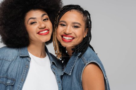 Photo for Young and happy african american girlfriends in blue denim clothes looking at camera on grey - Royalty Free Image