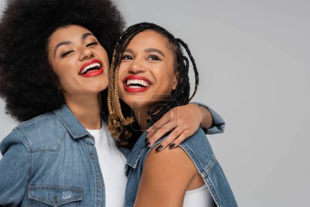 Photo for Excited and stylish african american woman embracing girlfriend on grey backdrop, denim style - Royalty Free Image