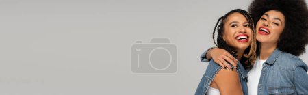 Photo for Laughing african american woman embracing girlfriend in denim clothes on grey backdrop, banner - Royalty Free Image