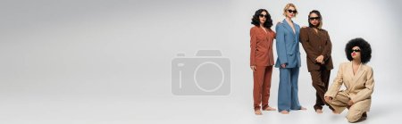 Téléchargez les photos : Afro-américaine sur des hanches près de copines multiethniques en lunettes de soleil et costumes, bannière - en image libre de droit