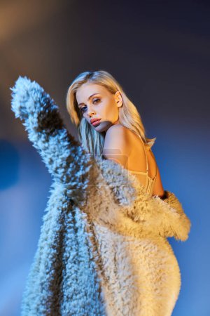 vertical shot of appealing young woman in white faux fur coat turning her head and looking at camera