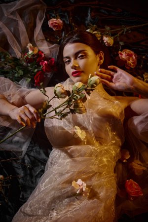 weibliche Eleganz, brünette junge Frau in romantischem transparentem Kleid zwischen schönen Blumen liegend