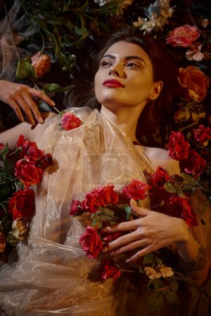 weibliche Anmut, tätowierte Frau in romantischem transparentem Kleid, die zwischen wunderschönen Blumen liegt