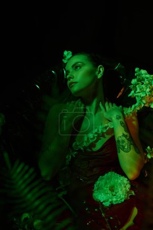 grünes Licht, verträumte junge Frau mit nassen Haaren, die wegschaut und zwischen Blumen posiert, Eleganz