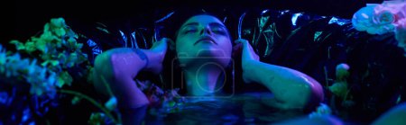 blue light banner, sensual and young woman with wet hair diving into water in bathtub with flowers