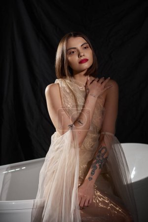 elegancia femenina, mujer joven soñadora en vestido romántico de pie cerca de la bañera blanca en negro