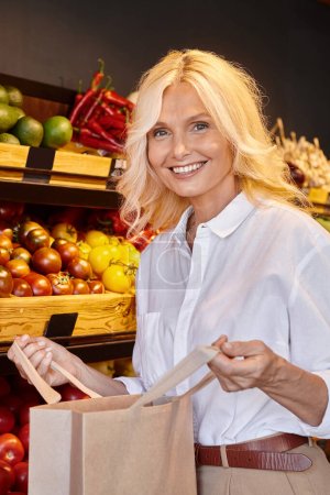 Ältere Frau in Freizeitkleidung posiert mit offener Einkaufstasche mit Marktstand im Hintergrund