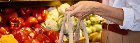 cropped view of mature female in casual attire holding shopping bag at grocery store, banner