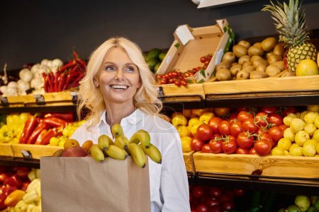fröhliche Seniorin posiert mit Einkaufstasche voller frischer Früchte und schaut weg
