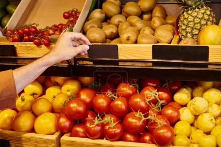 Téléchargez les photos : Vue recadrée du vendeur mâle mature mettant l'étiquette de prix sur l'étal d'épicerie avec des fruits et légumes - en image libre de droit