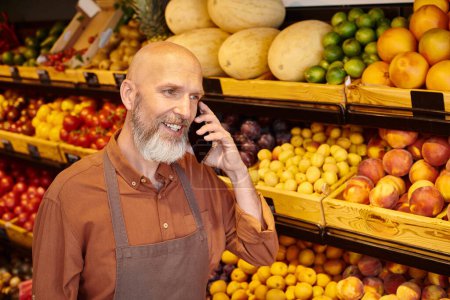Ältere gut aussehende Verkäuferin mit Bart telefoniert in der Pause von der Arbeit im Lebensmittelgeschäft