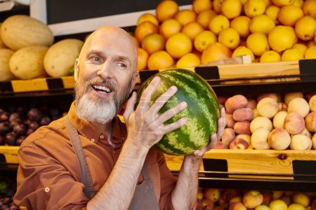 cheerful bearded salesman posing with happily with watermelon near head and smiling joyfully