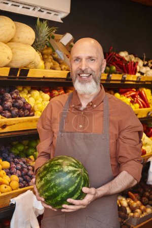 vertical shot of gray bearded jolly salesman posing with watermelon in hands and smiling at camera