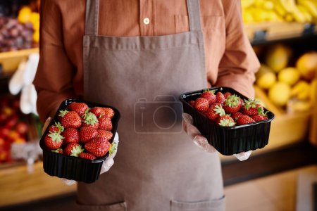 cropped view of mature salesman holding packs of delicious fresh strawberries at grocery store