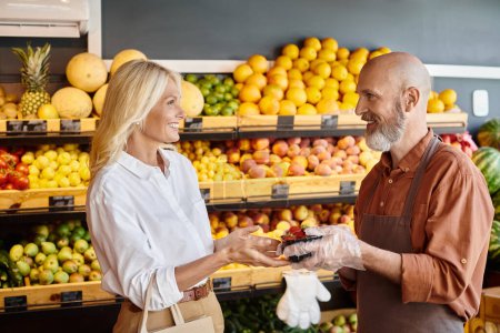 Photo for Cheerful bearded seller giving pack of strawberries to his jolly customer, smiling at each other - Royalty Free Image