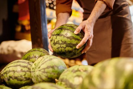 Photo for Cropped view of mature cheerful seller with beard picking huge fresh watermelon at grocery store - Royalty Free Image