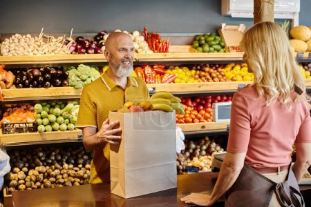 focus on mature customer buying fresh fruits and smiling at blurred female seller at grocery shop