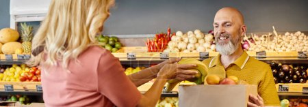 Photo for Focus on smiling man looking at blurred female seller putting fresh bananas into paper bag, banner - Royalty Free Image