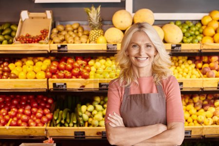 good looking jolly seller posing with arms crossed on chest and smiling at camera at grocery store