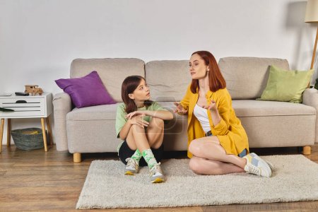 Mutter gestikuliert und spricht über Sexualerziehung mit aufmerksamer Teenager-Tochter in der Nähe von Laptop auf dem Boden