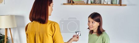 Photo for Mother showing condom to confused teenage daughter at home, sex education, horizontal banner - Royalty Free Image