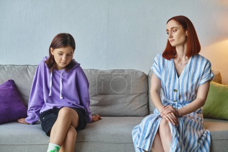 Photo for Thoughtful woman looking at frustrated teenage daughter on couch in living room, care and support - Royalty Free Image