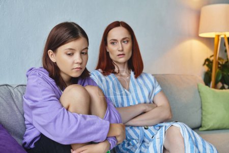 Photo for Worried mother looking at depressed teenage daughter on couch in living room, supportive parent - Royalty Free Image