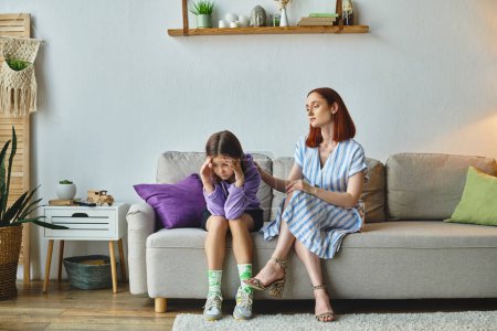 worried mother calming depressed teenage daughter sitting with bowed head on couch at home, support