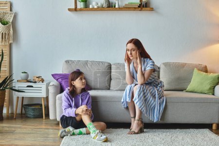 Frustrierte Frau berührt Kopf nahe Teenager-Tochter sitzt auf dem Boden im Wohnzimmer, Konflikt