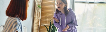 irritated teenage girl screaming and quarreling with mother at home in living room, banner