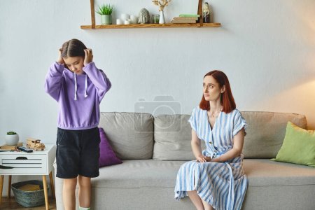 Photo for Offended teenage girl covering ears with hands near upset mother sitting on couch, generation gap - Royalty Free Image
