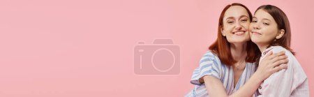 mujer alegre y de moda con hija adolescente abrazando y mirando a la cámara en rosa, pancarta