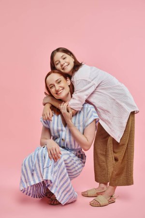 Photo for Happy teenage girl embracing stylish mother posing on haunches on pink backdrop, love and unity - Royalty Free Image