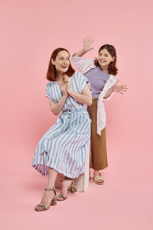 fröhliche Teenie-Mädchen Spaß haben und erschrecken Mutter sitzt auf Steinblock auf rosa Hintergrund
