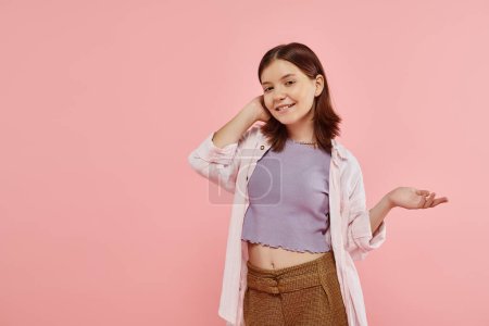 fröhliches Teenager-Mädchen in stylischer Freizeitkleidung zeigt mit der Hand und blickt in die Kamera auf rosa