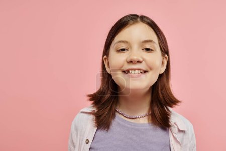 portrait of carefree and happy teenage girl with radiant smile looking at camera on pink backdrop