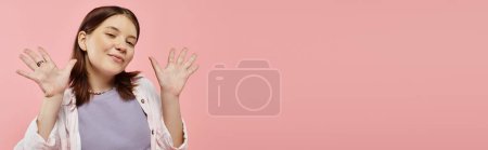 fröhliches Teenager-Mädchen in stilvoller Freizeitkleidung winkt mit den Händen und blickt in die Kamera auf rosa, Banner
