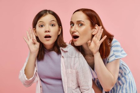 Neugierige Mutter und Teenager-Tochter halten sich die Hände an den Ohren und belauschen auf rosa Hintergrund