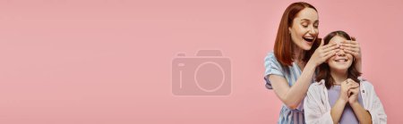 Téléchargez les photos : Joyeuse femme couvrant les yeux de la fille préadolescente tout en jouant devinez qui jeu sur fond rose, bannière - en image libre de droit